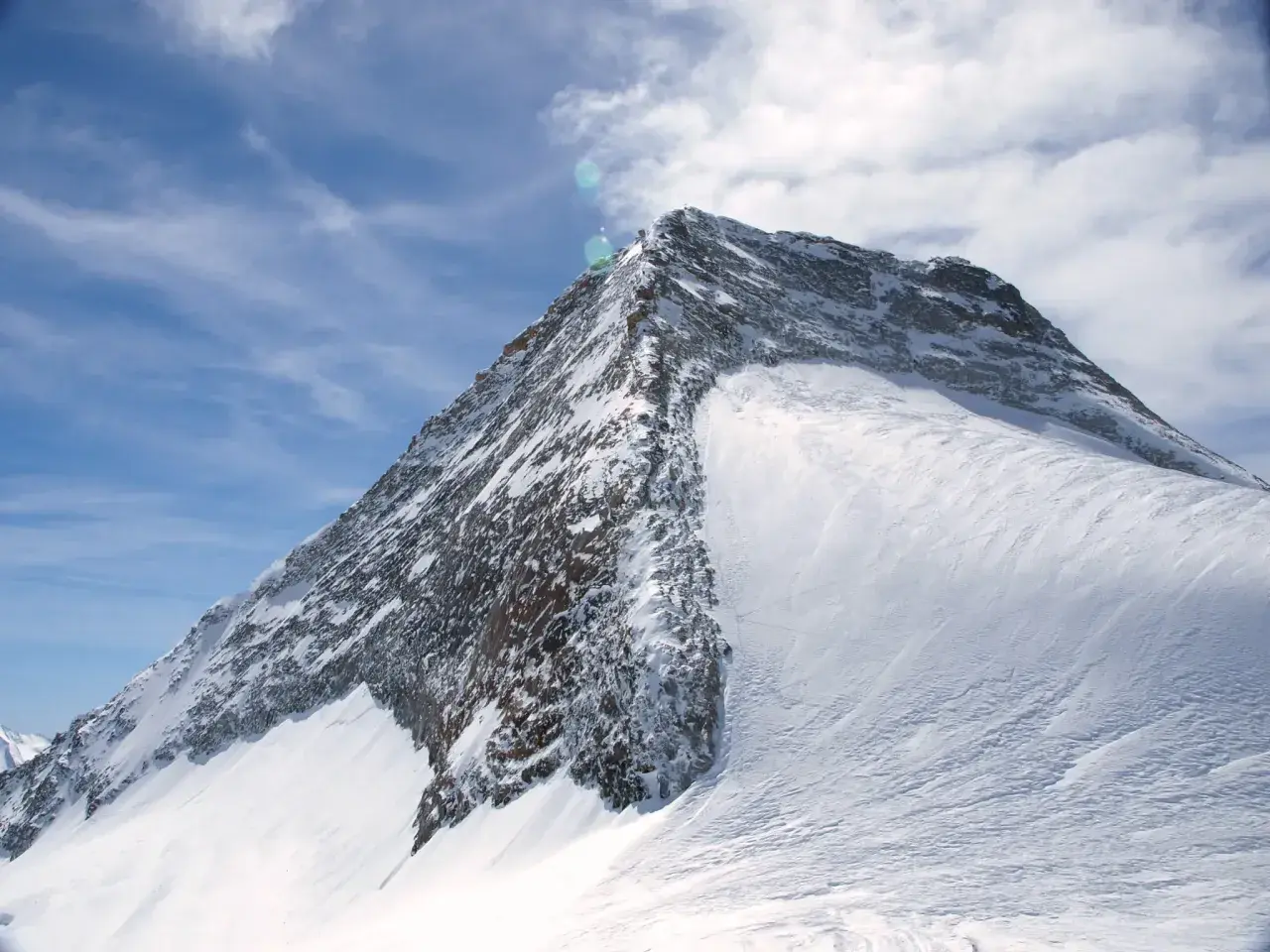 Der majestätische Olperer Nordgrat, bedeckt mit glitzerndem Schnee, ragt unter einem strahlend blauen Himmel mit zarten Wolken empor.