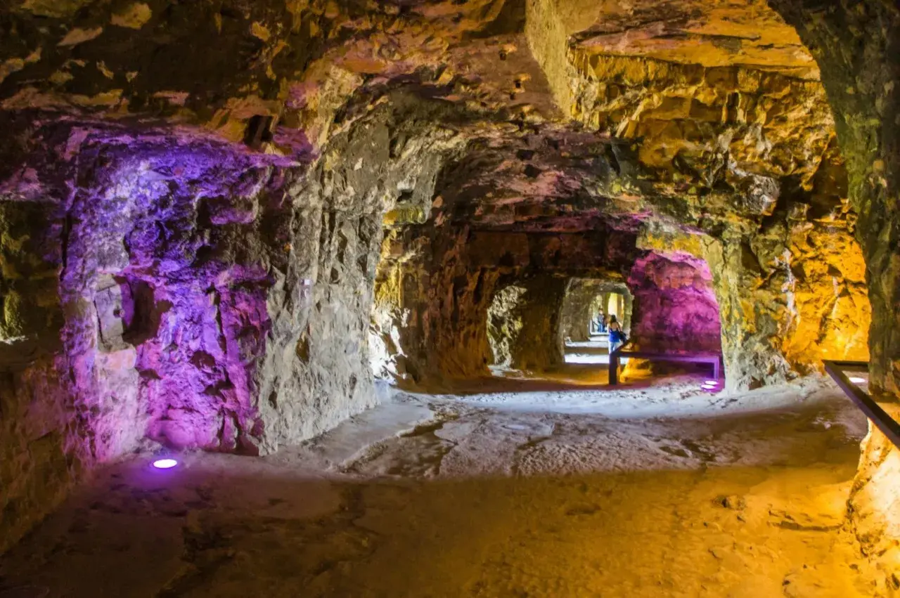 Beleuchtete Gänge der Kasematten Luxemburg, mit lila und gelbem Licht, das die rauen Steinwände hervorhebt.