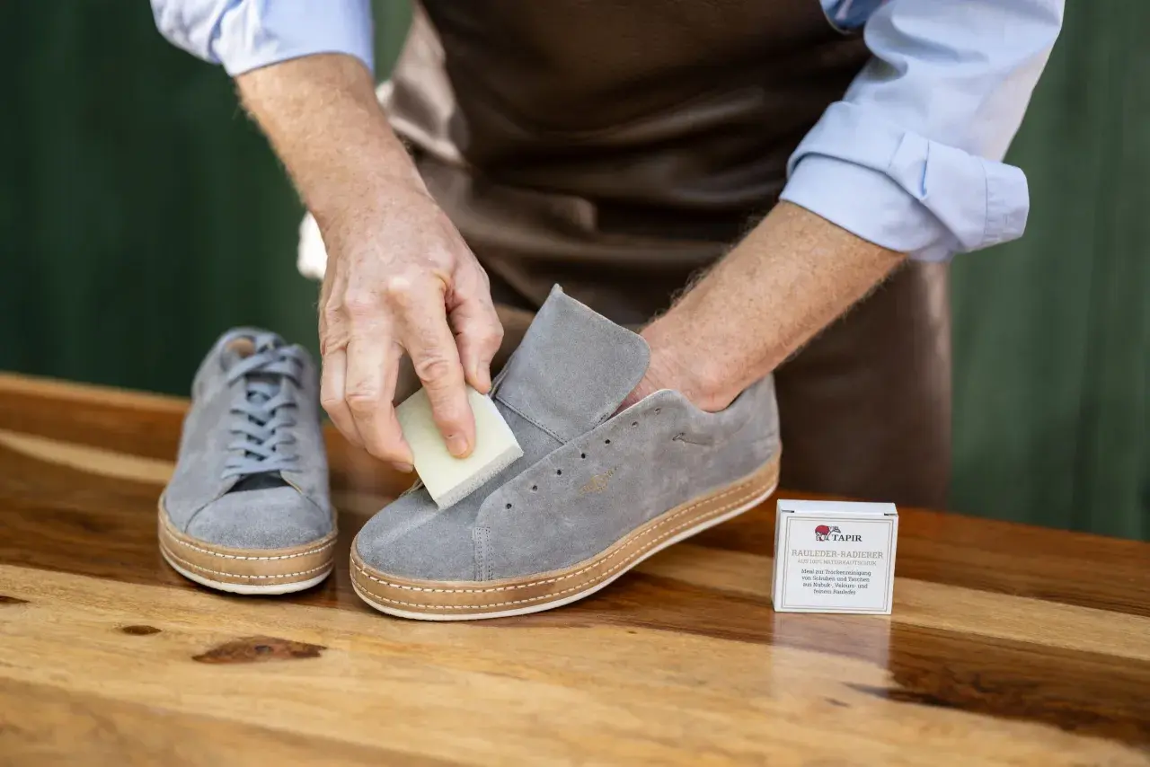 Mann reinigt graue Nubukleder-Sneaker mit einem speziellen Radierer. Die richtige nubukleder pflege erhält die Schuhe.