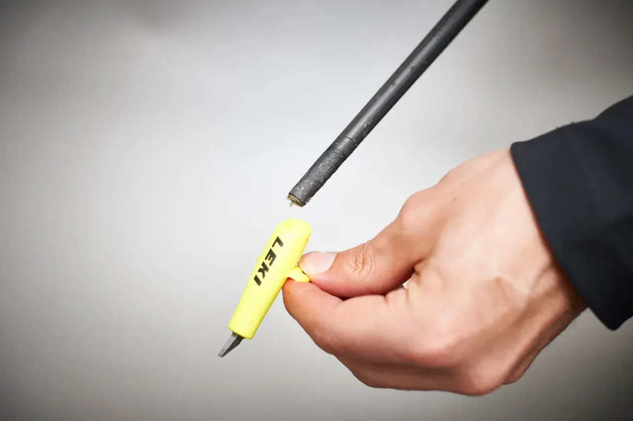 Hand hält gelbes Werkzeug mit "LEKI" Schriftzug, um die Spitze eines Skistocks zu wechseln.