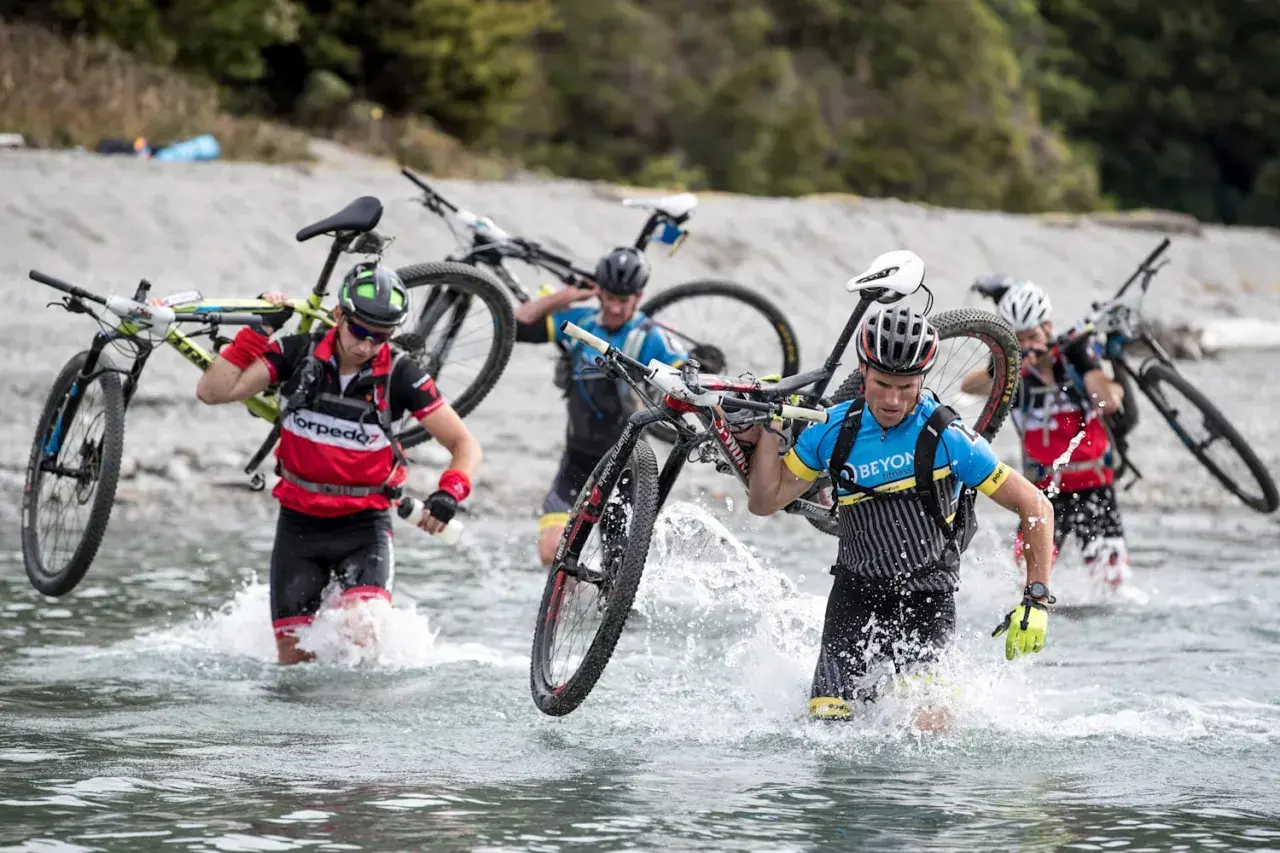 Teilnehmer eines **adventure racing** durchqueren mit ihren Mountainbikes einen Fluss.