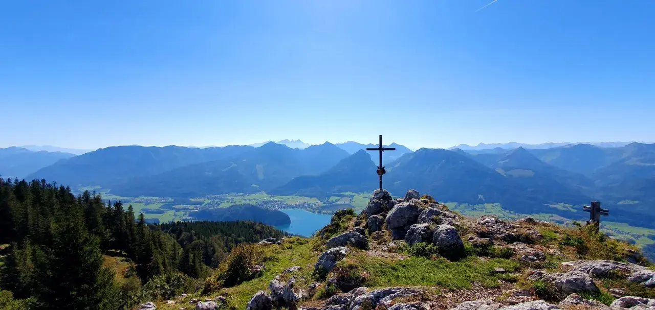 Gipfelkreuz mit Blick auf einen See und Berge. Perfekt für Salzkammergut wandern.