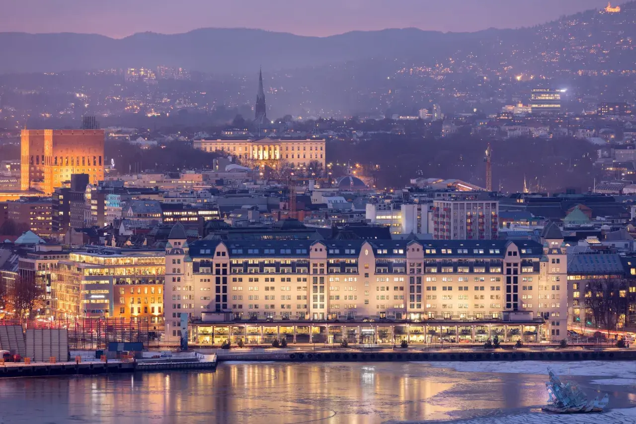 Oslo bei Nacht: beleuchtete Gebäude am Wasser, im Hintergrund die Stadt und Berge. Ein Muss für jeden Oslo-Besucher!