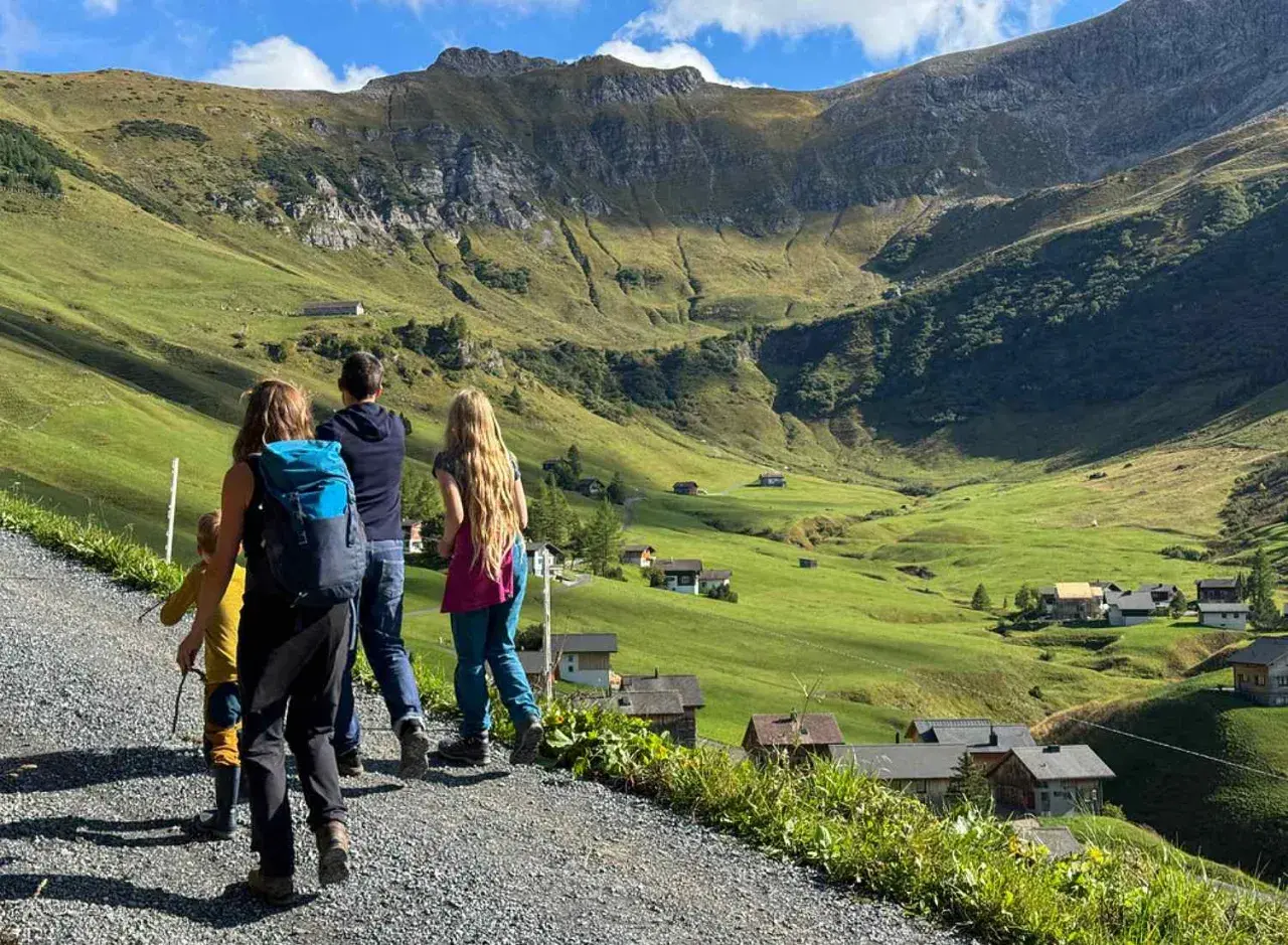 Familie genießt das Liechtenstein wandern in den Alpen. Grüne Hänge, kleine Häuser und ein Bergpanorama.