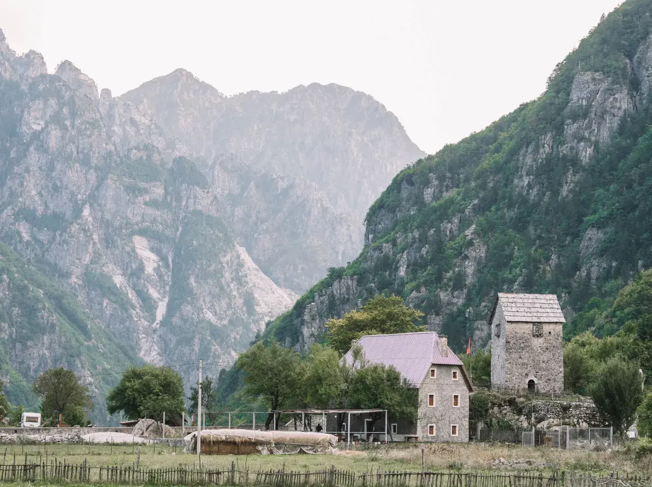 Steinerne Häuser und ein alter Turm in Albanien Theth, umgeben von majestätischen, nebelverhangenen Bergen.