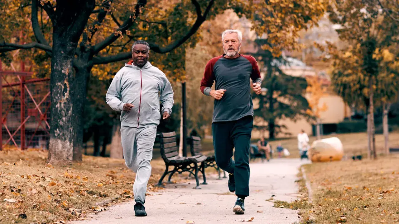 Zwei Männer im Herbstpark trainieren für den Halbmarathon. Sie laufen auf einem Weg, umgeben von bunten Blättern.