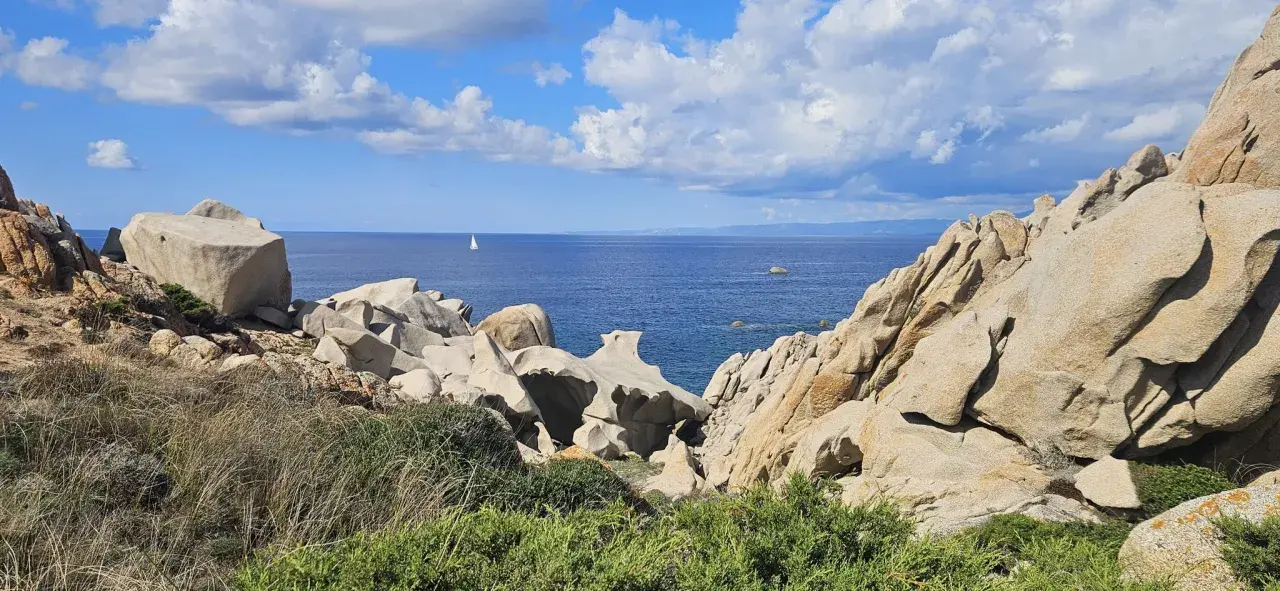 Felsformationen am Capo Testa, Sardinien, mit Blick auf das blaue Meer und eine einsame Segelyacht.
