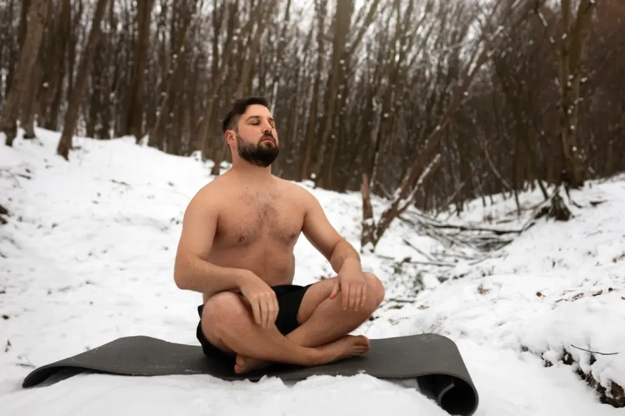 Mann in der Natur, barbusig im Schnee sitzend, praktiziert Wim Hof Atmung.