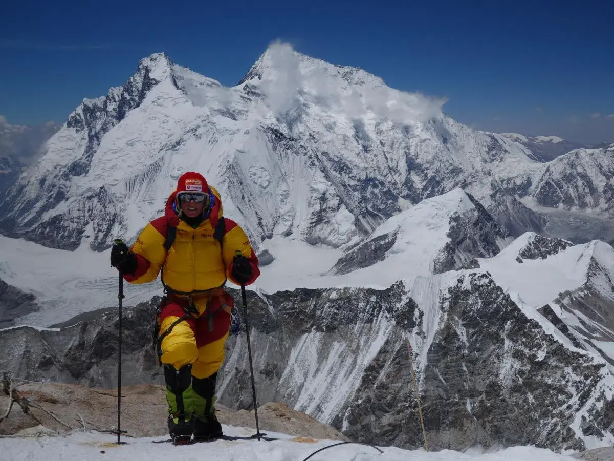 Alix von Melle, in voller Bergsteigerausrüstung, steht auf einem schneebedeckten Gipfel vor einer majestätischen Bergkulisse.
