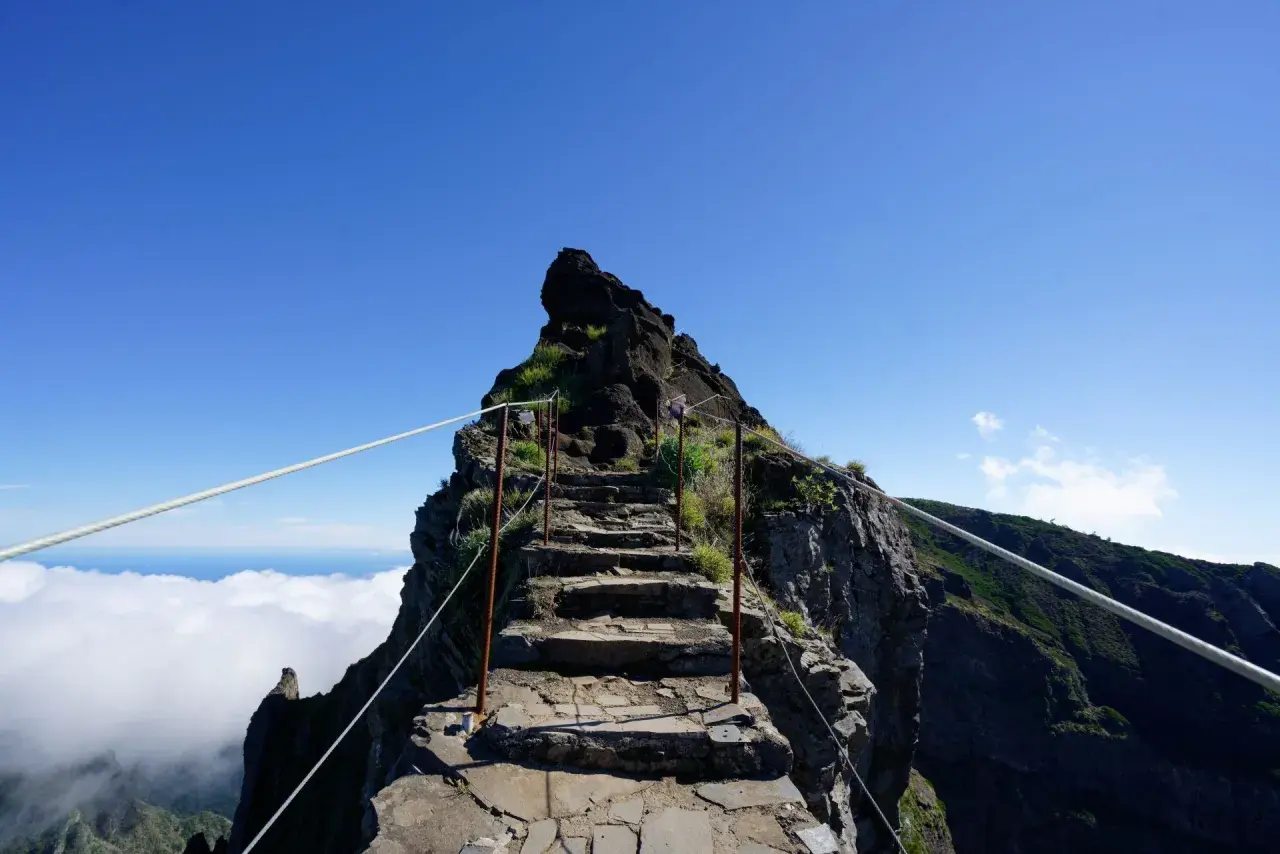 Steile Steintreppe, die sich den Berg hinaufwindet, mit Seilen gesichert. Eine Himmelsleiter auf Madeira, die über den Wolken in den blauen Himmel führt.