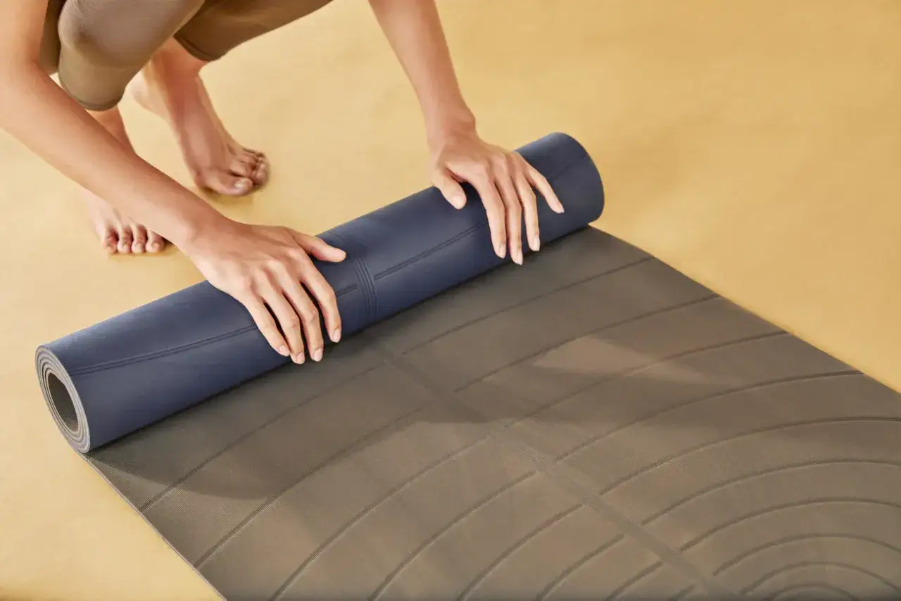 H&auml;nde rollen eine dunkelblaue Naturkautschuk Yogamatte auf, um sie zu reinigen.
