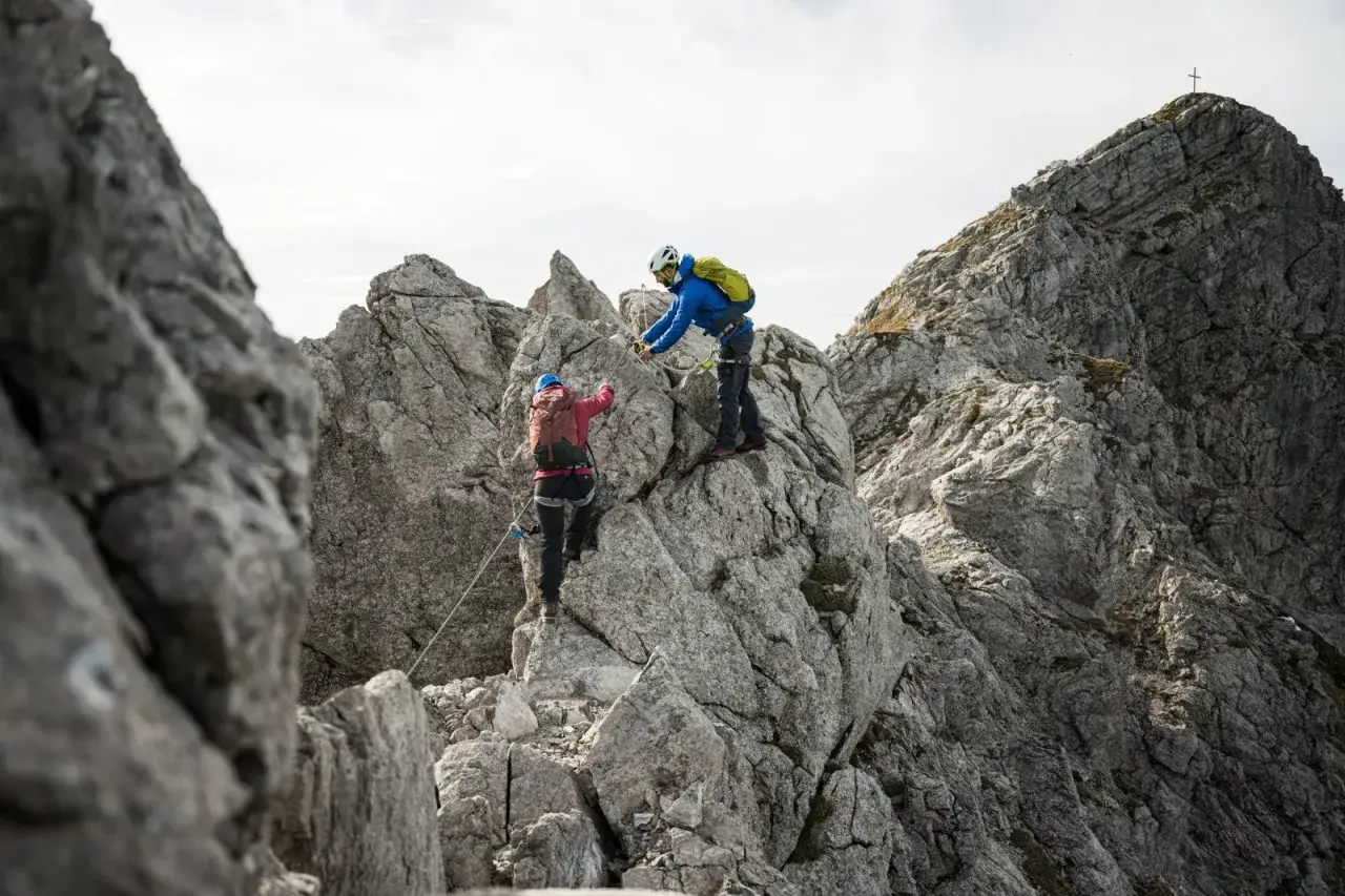 Zwei Kletterer meistern einen anspruchsvollen Klettersteig bei Oberstdorf. Sie sichern sich an Stahlseilen und erklimmen felsige Abschnitte.
