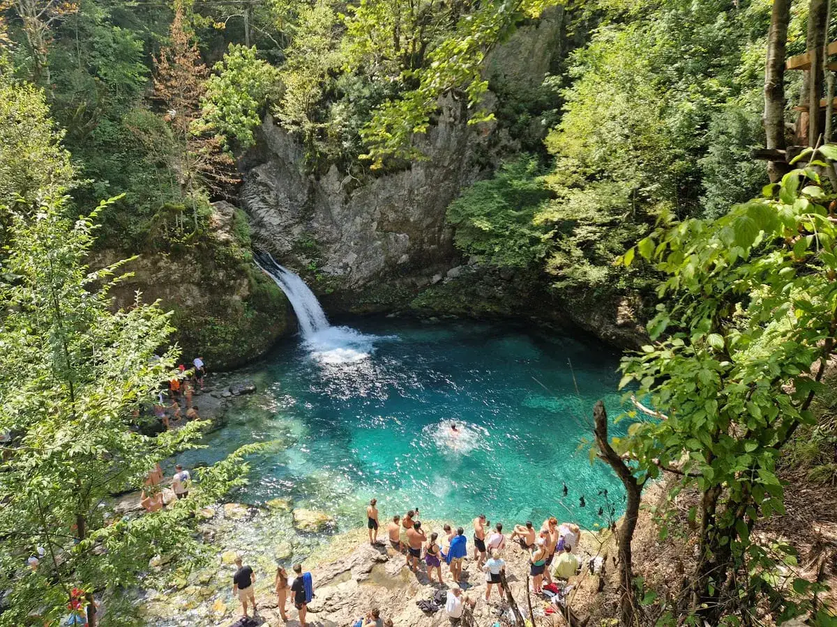 T&uuml;rkisblaue Lagune mit Wasserfall in Albanien, Theth. Menschen genie&szlig;en das k&uuml;hle Wasser inmitten &uuml;ppiger Natur.