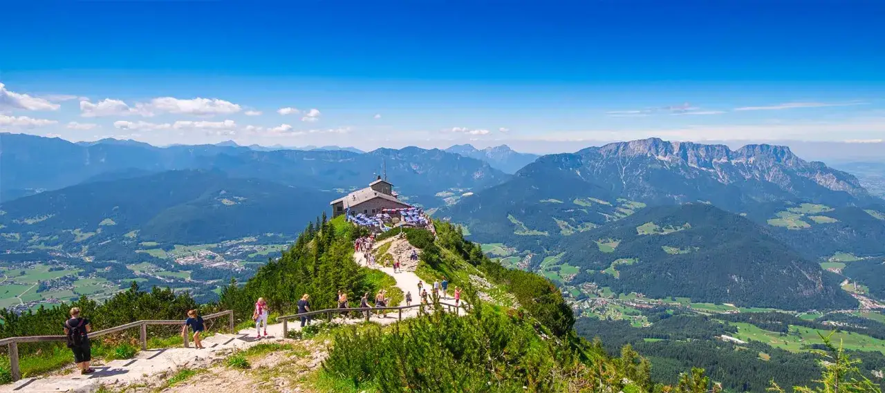 Blick auf das Kehlsteinhaus auf einem Berggipfel, umgeben von gr&uuml;nen T&auml;lern und majest&auml;tischen Alpen. Eine Wanderung hierher lohnt sich!