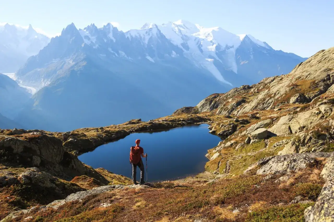 Wanderer mit Rucksack und St&ouml;cken blickt auf Bergsee. Majest&auml;tische Alpenkulisse, ideal f&uuml;r mehrtageswanderungen.