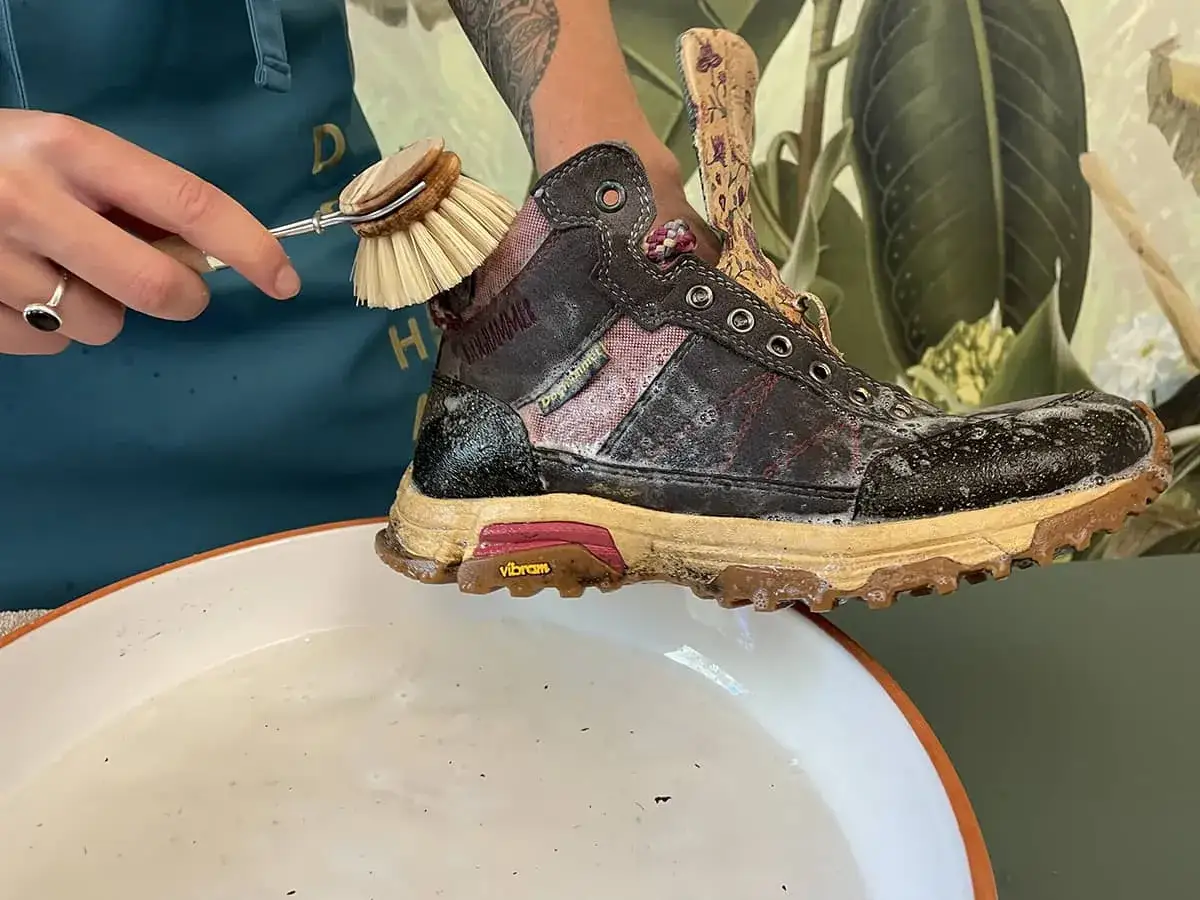 Mit einer B&uuml;rste werden schmutzige Wanderschuhe in Seifenwasser gereinigt.
