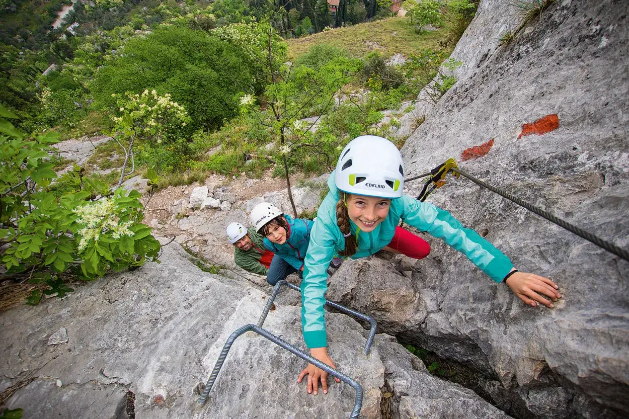 Glückliche Kinder und ein Mann klettern einen Klettersteig mit Stahlseilen und Trittbügeln. Ein spannendes Abenteuer für die ganze Familie.
