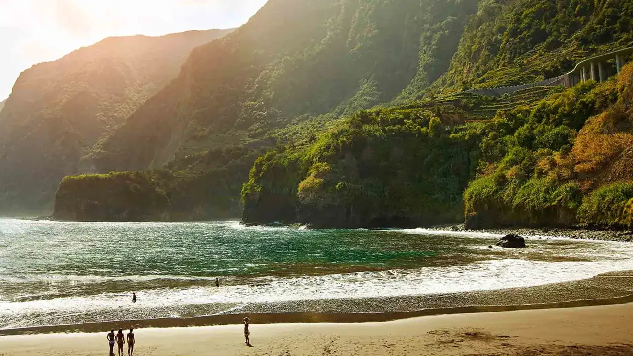 Ein malerischer madeira schwarzer strand mit sanften Wellen und üppig grünen Bergen im Hintergrund. Ein paar Menschen genießen die Sonne.