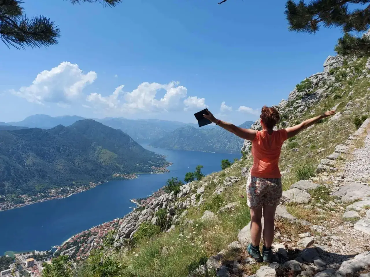 Frau mit ausgebreiteten Armen genie&szlig;t den atemberaubenden Blick auf die Bucht von Kotor. Ein perfekter Moment f&uuml;r ihren Reisebericht Montenegro.