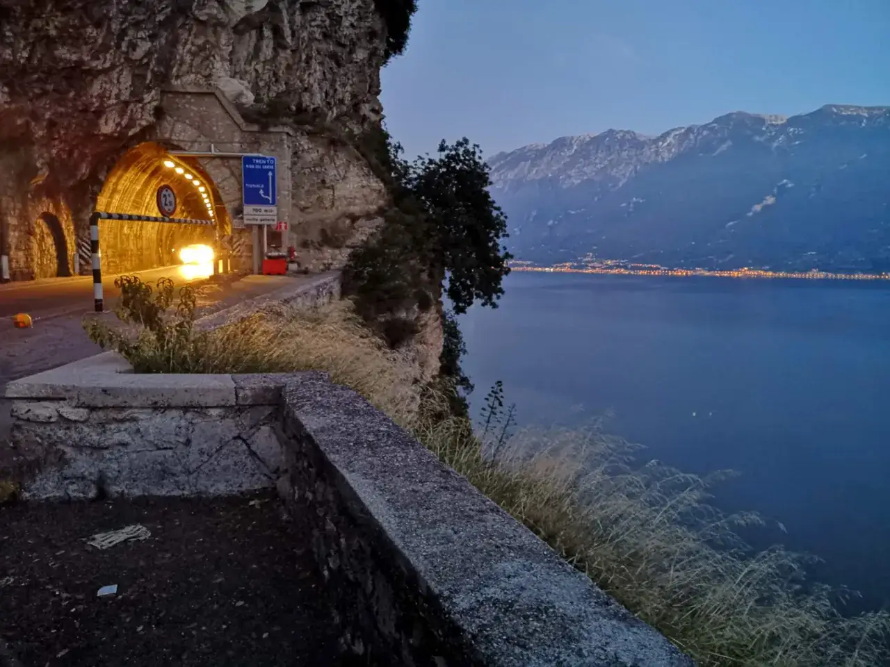 D&auml;mmerung am Gardasee: Ein Tunnel beleuchtet die Stra&szlig;e, w&auml;hrend Lichter am Ufer funkeln. Perfekt f&uuml;r abendliche Gardasee Unternehmungen.