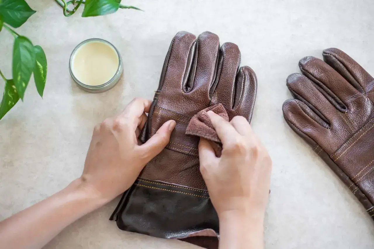 H&auml;nde polieren braune lederhandschuhe mit einem Tuch. Daneben steht ein Glas mit Pflegecreme.