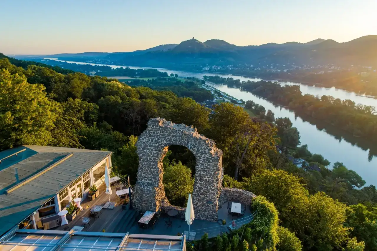 Der Rolandbogen thront über dem Rhein. Eine Ruine mit Blick auf Berge und Fluss, umgeben von grünen Wäldern.