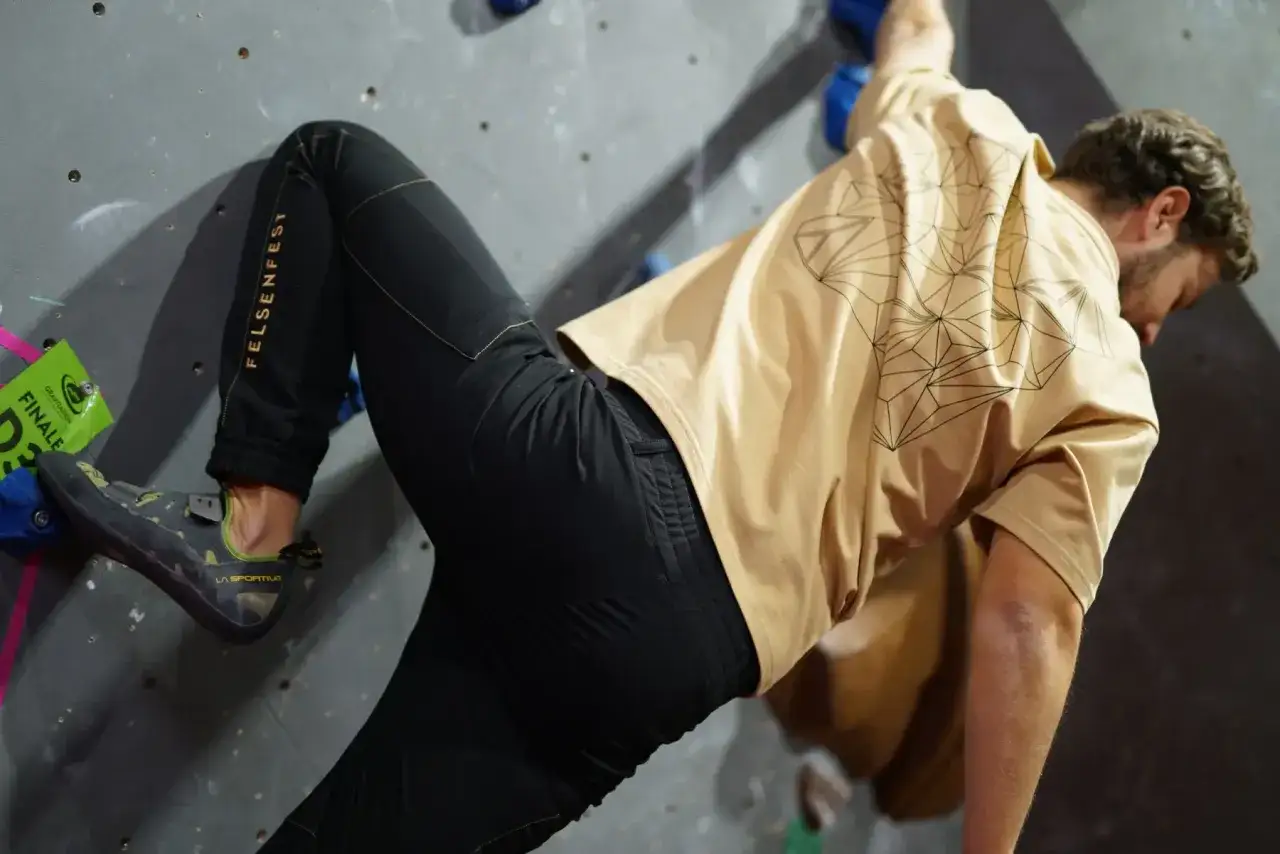 Mann in beiger Shirt und schwarzer Hose beim Bouldern. So zieht man zum Bouldern an: bequeme Kleidung für maximale Bewegungsfreiheit.