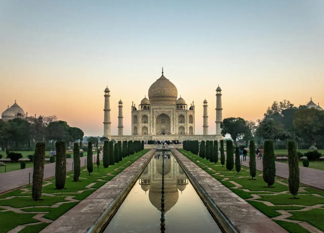 Der Taj Mahal spiegelt sich im Wasser. Ein majestätisches Mausoleum in Indien, umgeben von Gärten und Zypressen.