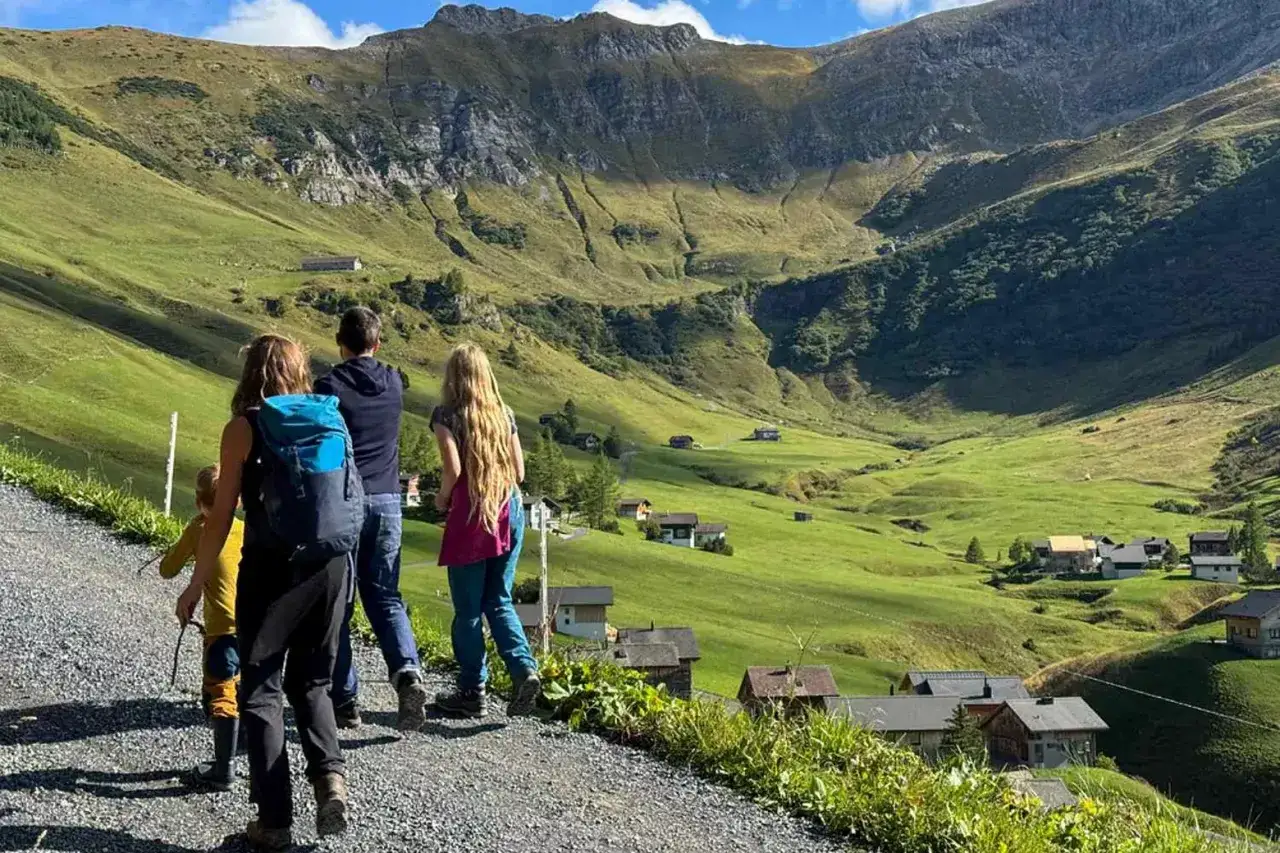 Familie genießt das Liechtenstein Wandern in einem malerischen Tal mit traditionellen Häusern und steilen Berghängen.