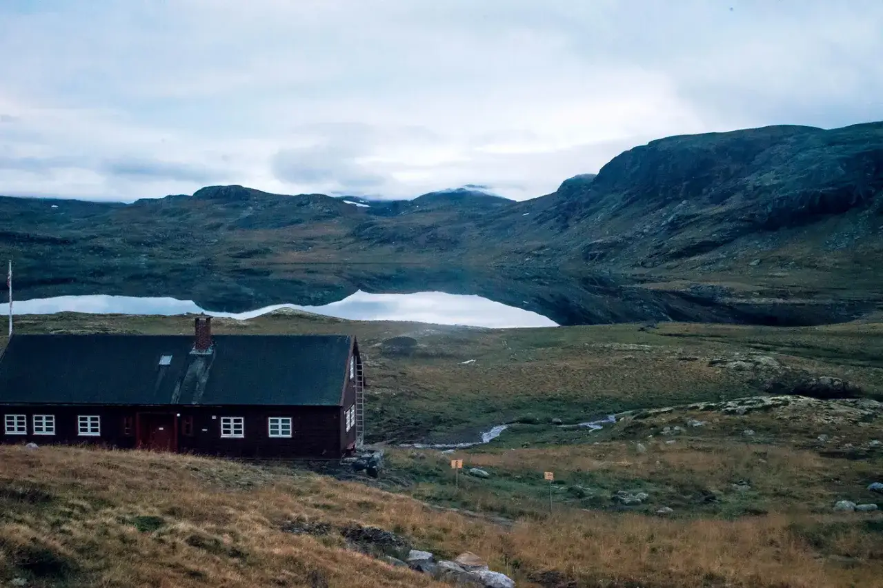 Ein einsames Haus am See, bereit für das nächste Abenteuer beim Hardangervidda wandern. Berge spiegeln sich im ruhigen Wasser.