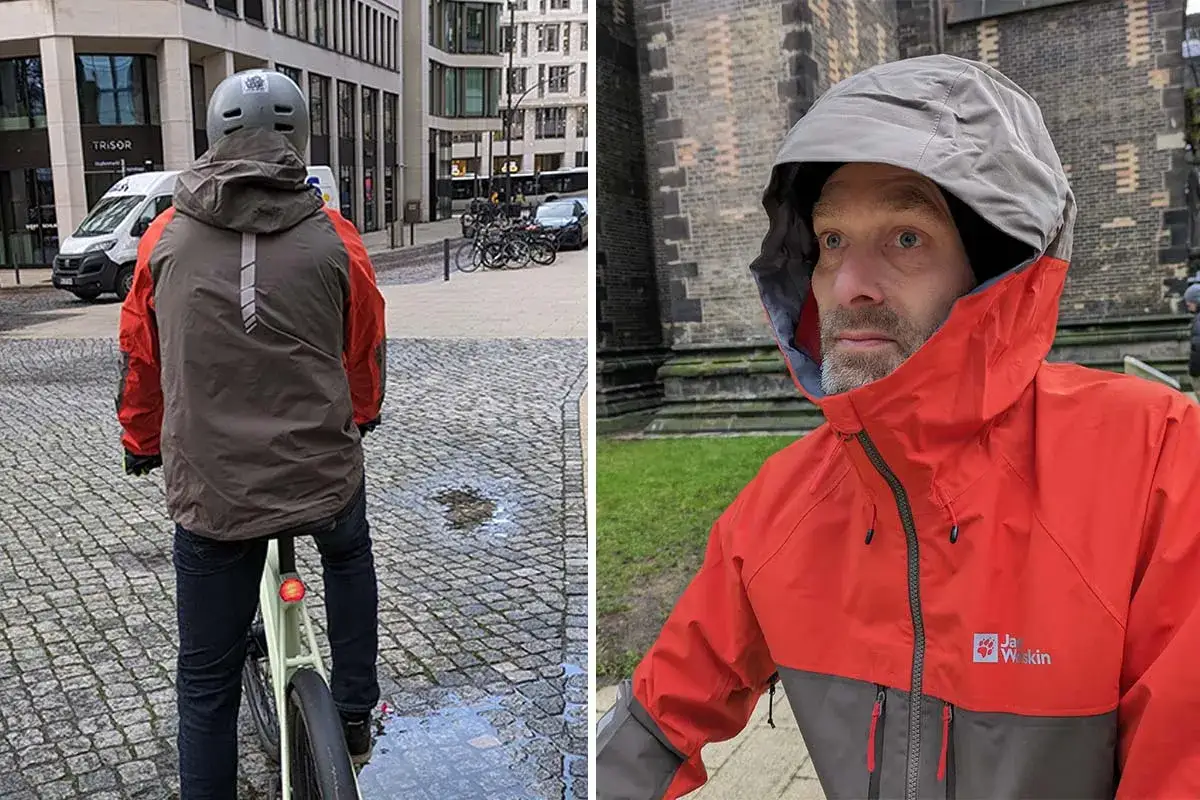 Mann in orange-grauer Jacke mit Kapuze, die den Unterschied zwischen wasserdicht und wasserfest demonstriert.