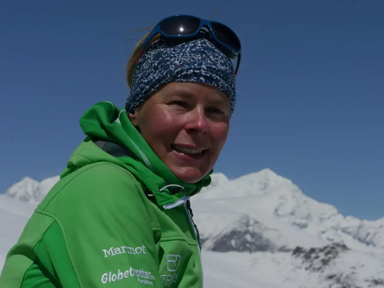 Alix von Melle lächelt in die Kamera, gekleidet in eine grüne Jacke, vor einer verschneiten Bergkulisse.