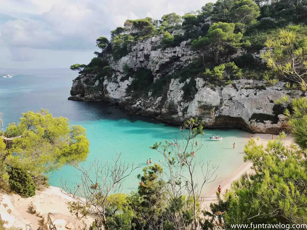Türkisblaues Wasser, weiße Felsen und grüne Pinien: Ein idyllischer Strand auf Menorca, der zu den Highlights der Insel zählt. Menschen genießen das Meer und die Sonne.