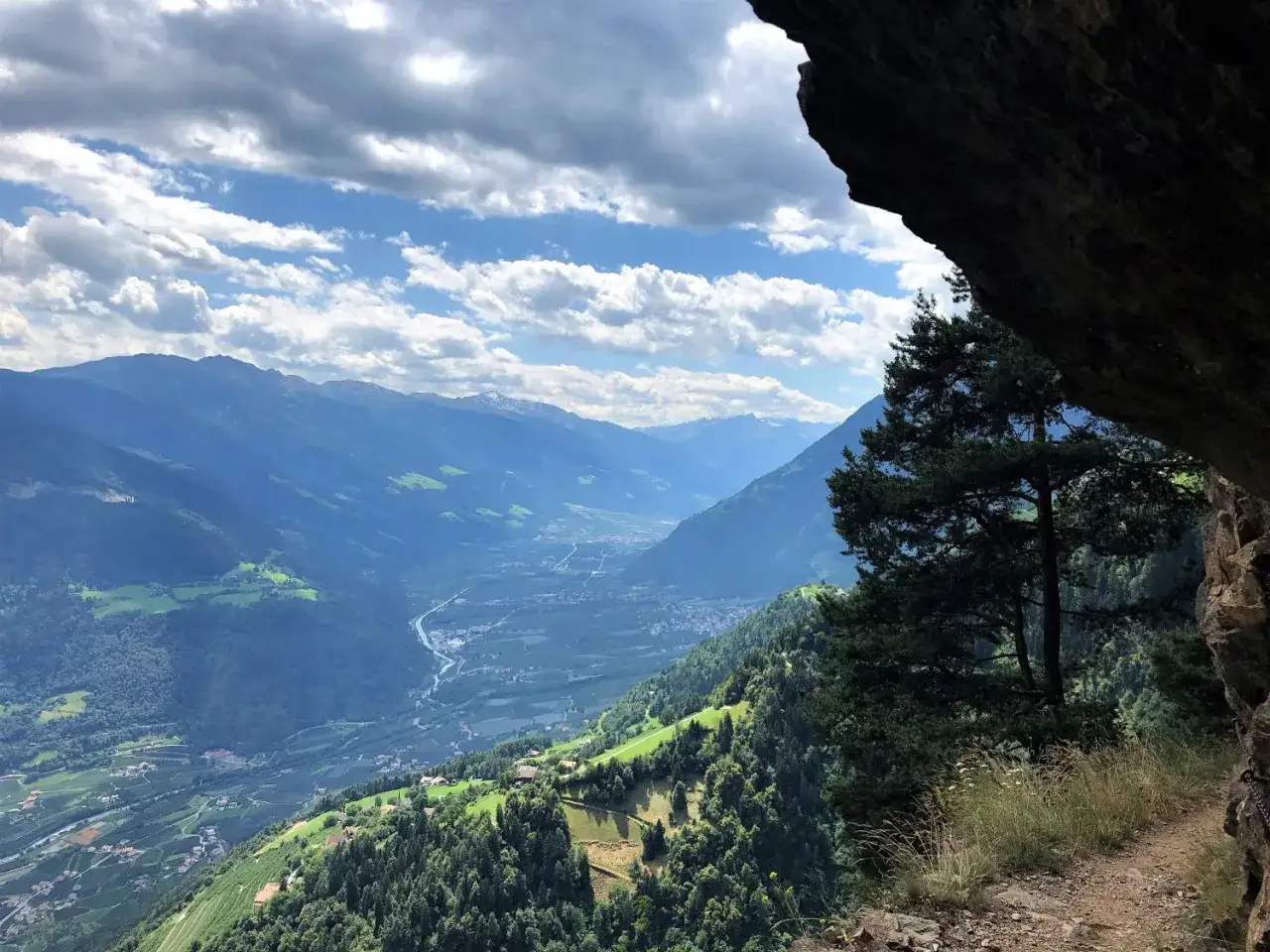 Blick aus einer Felsnische auf ein grünes Tal mit Bergkette. Ein Baum ragt ins Bild. Perfekt für hiking deutsch.