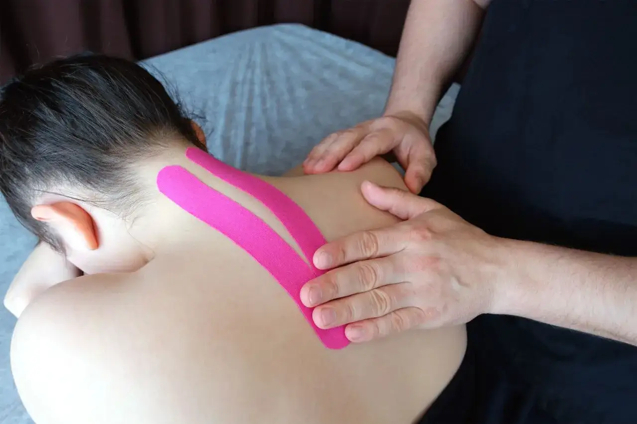 Therapeut wendet pinkes Kinesio-Tape am Nacken einer Person an, um Schmerzen zu lindern.