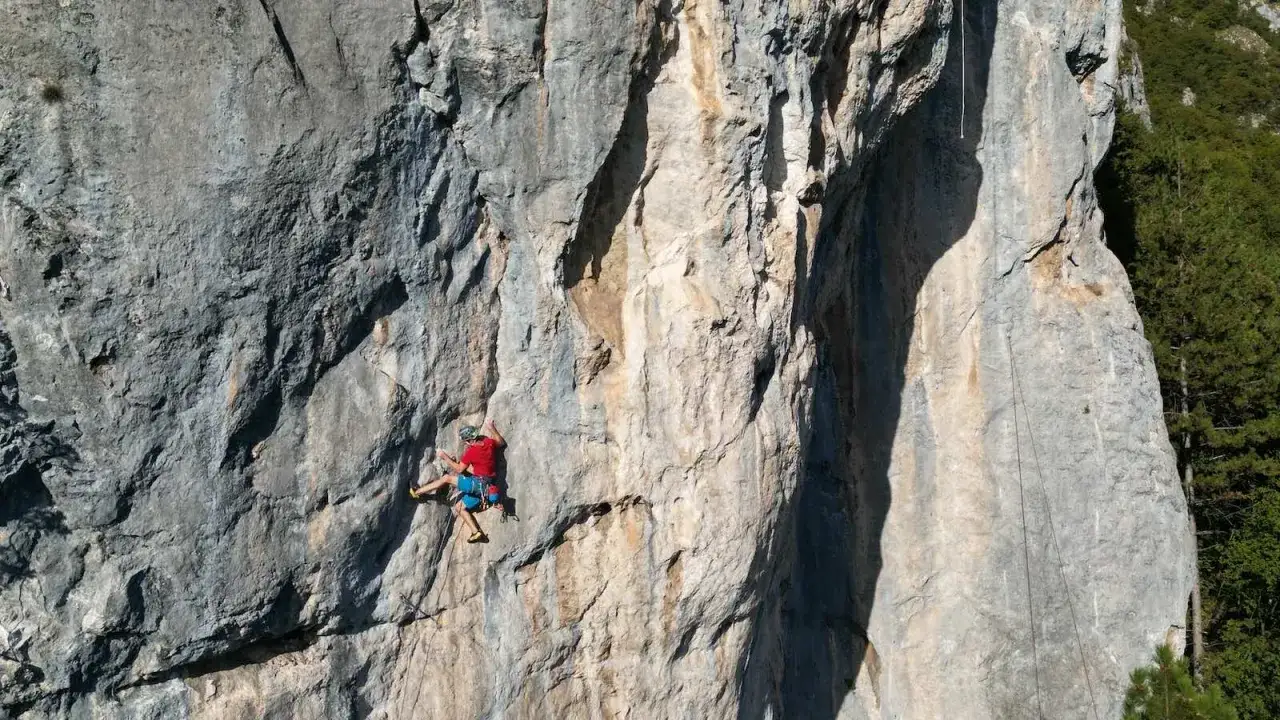 Ein Mann klettert am Fels, gesichert durch ein Seil. Die Sonne wirft Schatten auf die steile Wand.