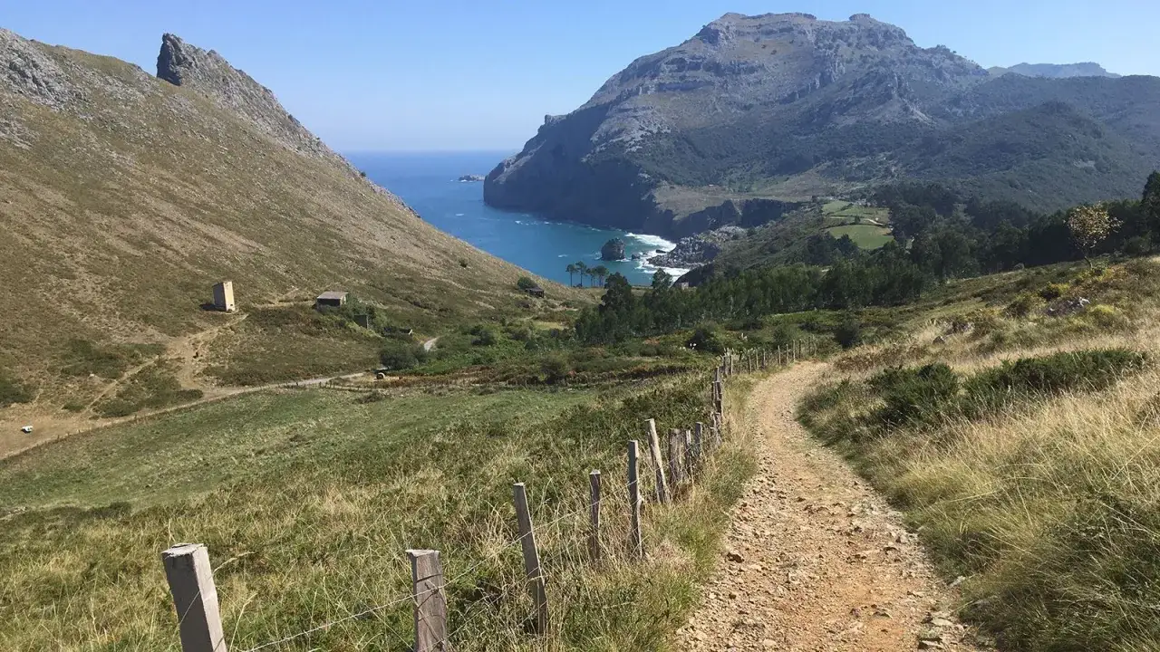 Ein schmaler Pfad führt durch grüne Hügel zum Meer. Der Jakobsweg Nordspanien verspricht atemberaubende Ausblicke und einsame Wege.