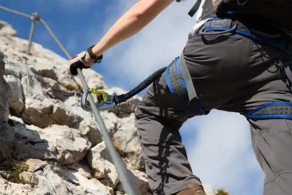 Person klettert gesichert an einem Stahlseil. Die Klettersteig Sicherung ist deutlich sichtbar.