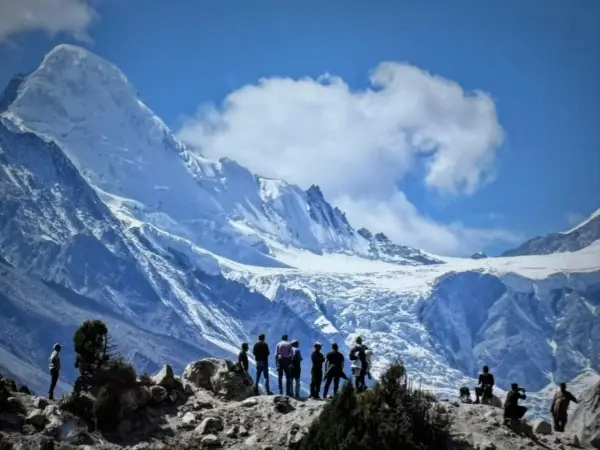 Bergsteiger bestaunen die majestätische Rupal-Wand, einen eisigen Riesen unter blauem Himmel.