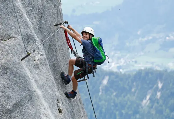 Ein Junge mit Helm und Rucksack klettert einen Felsgrat. Ein spannendes Abenteuer für klettersteig kinder.