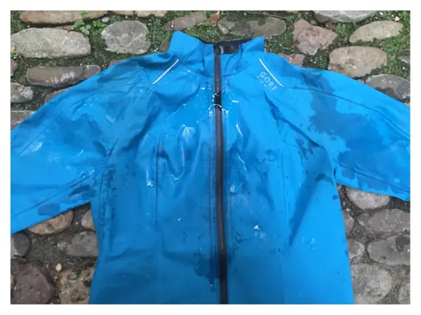 Blaue Gore-Tex Regenjacke mit Wasserflecken, bereit zum Trocknen auf einem steinigen Untergrund.